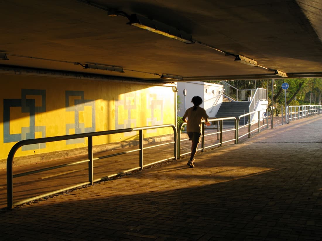 A runner passing through a city underpass in morning light