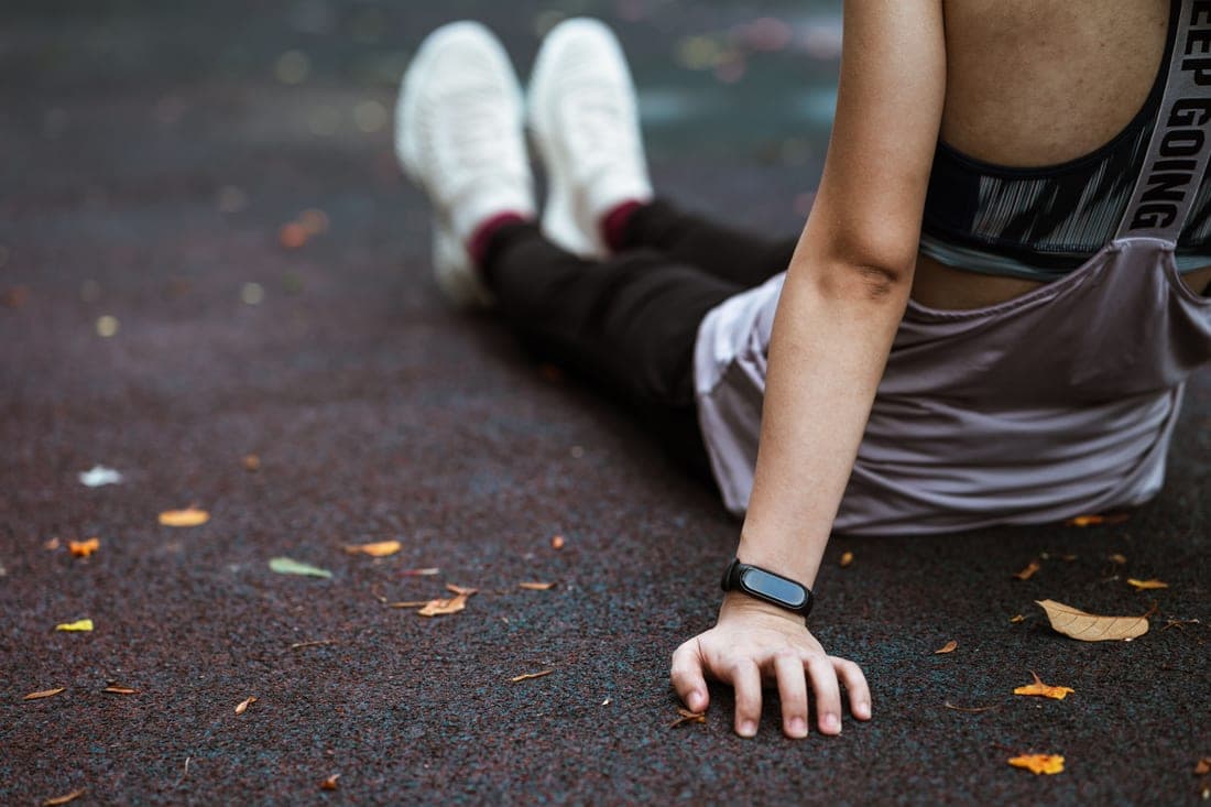 A runner wearing a sports watch resting on a track after a run
