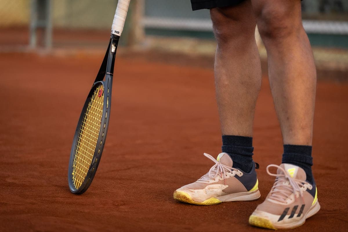 A tennis racket and court shoes on a clay tennis court