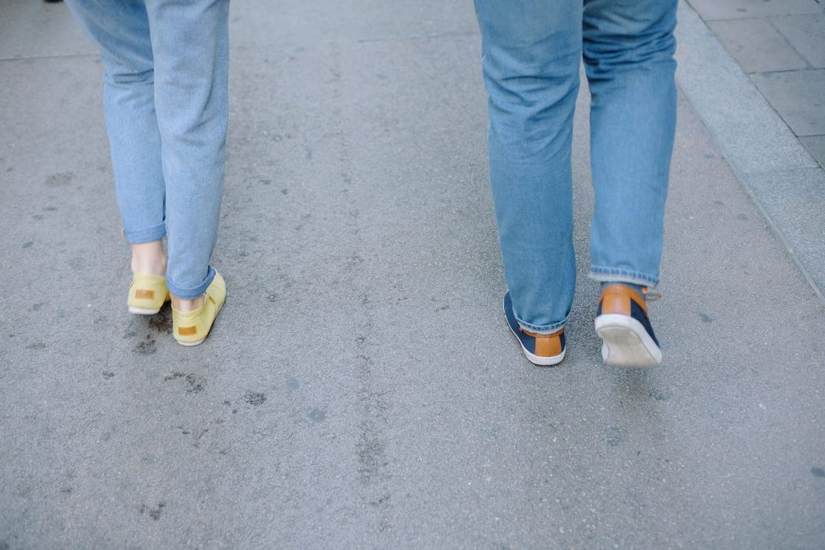 Two people in jeans and sneakers walking on a city sidewalk