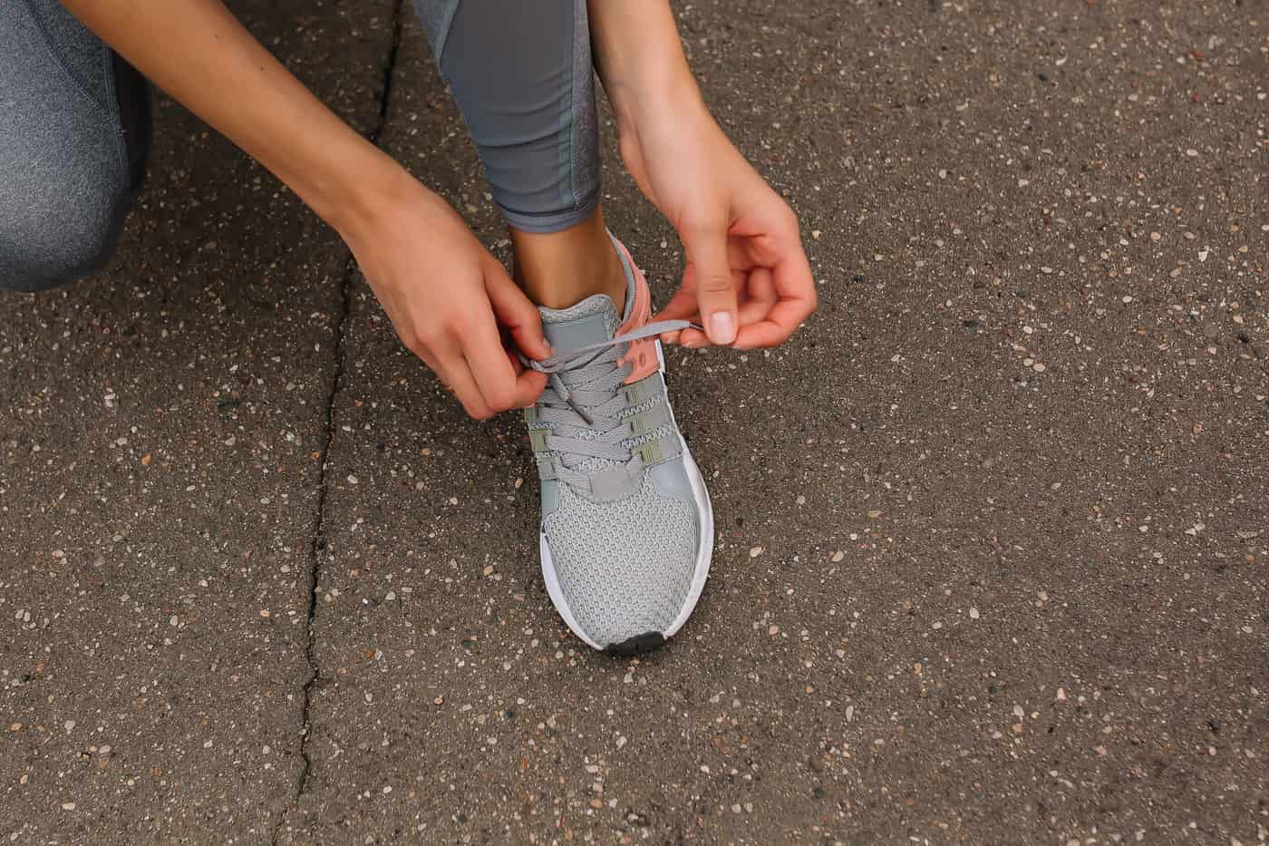 A runner tying the laces of a gray running shoe on pavement