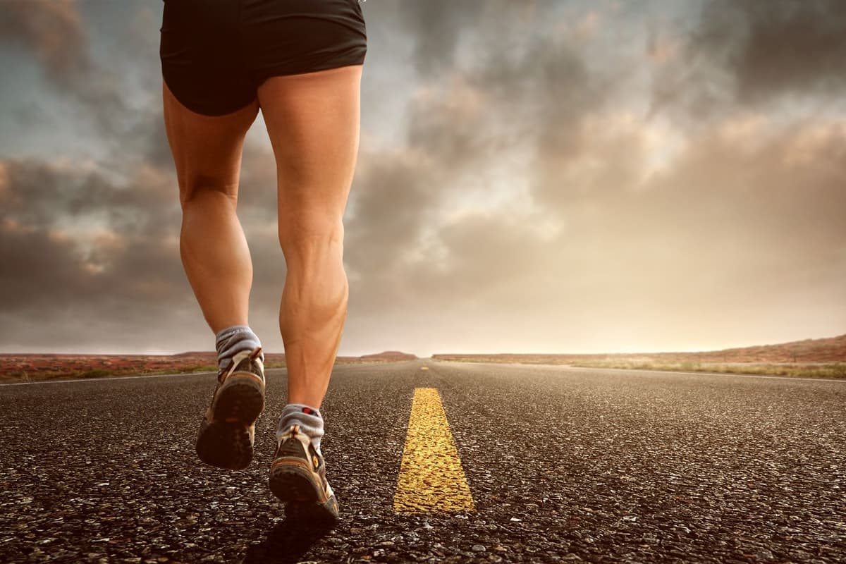 A runner's legs and shoes on an open road at sunset