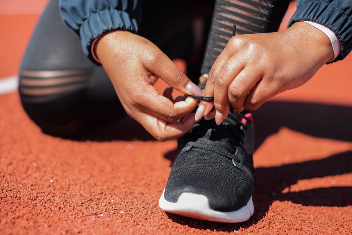 A runner tying black running shoes on a red track