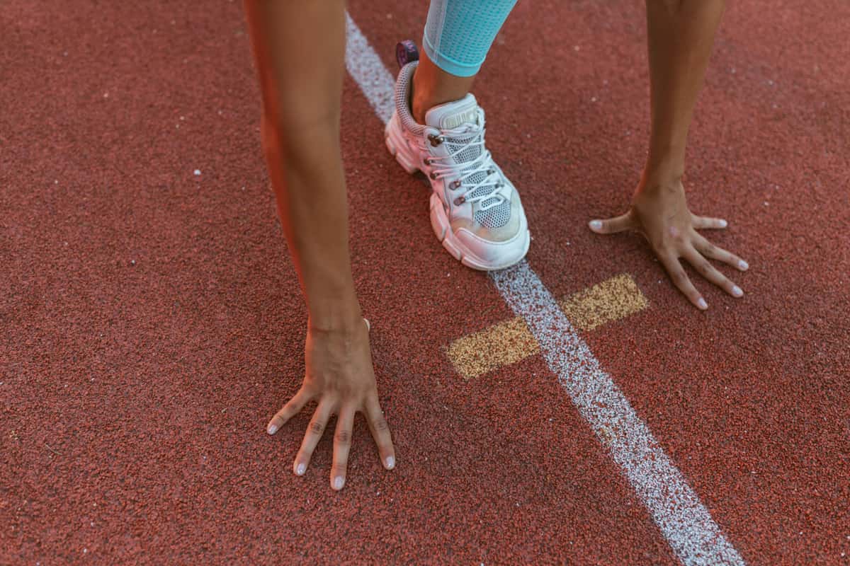 A runner's hand and shoe on the line of a red running track